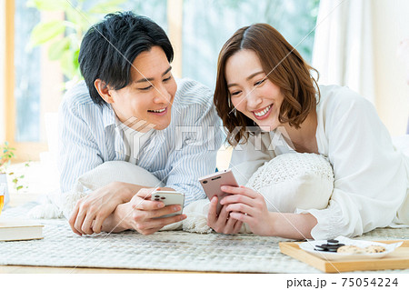 リビングでスマホを見る若い男女 リビングでスマホを見る若い男女 75054224