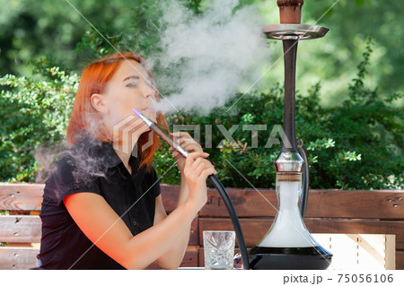 Young women smoke a hookah in a cafe on the street Young women smoke a hookah in a cafe on the street 75056106