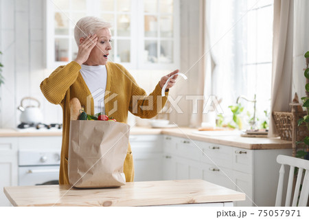 Amazed elderly woman checking grocery bill in kitchen 75057971