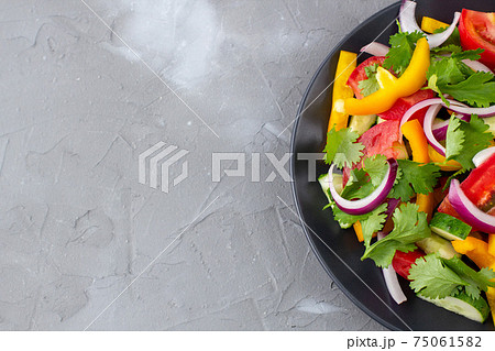 Plate of rainbow salad with different vegetables and herbs on black plate on grey stone background Plate of rainbow salad with different vegetables and herbs on black plate on grey stone background 75061582