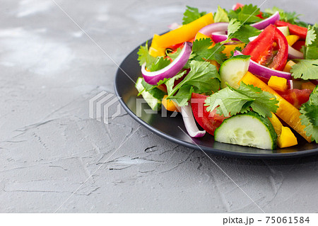 Plate of rainbow salad with different vegetables and herbs on black plate on grey stone background Plate of rainbow salad with different vegetables and herbs on black plate on grey stone background 75061584