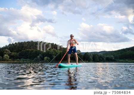 Senior man paddleboarding on lake in summer. Copy space. Senior man paddleboarding on lake in summer. Copy space. 75064834