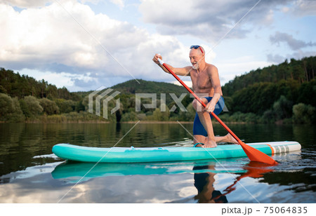 Senior man paddleboarding on lake in summer. Copy space. Senior man paddleboarding on lake in summer. Copy space. 75064835