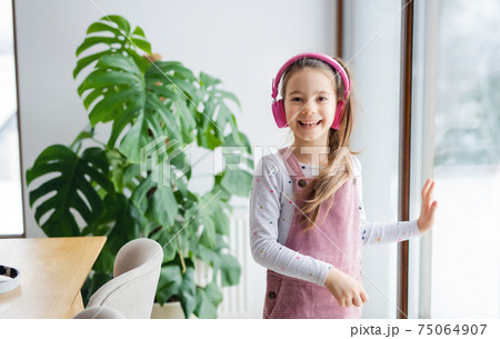 Small girl with headphones indoors at home, looking at camera. 75064907