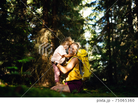 Happy mother with small daughter outdoors in summer nature, hugging and resting. 75065360