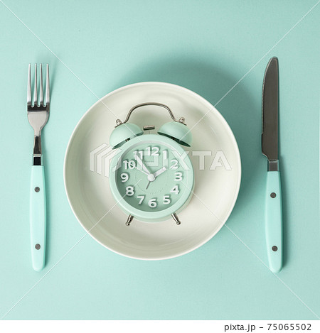 Composition with cutlery, plate and alarm clock on color background. Diet concept Composition with cutlery, plate and alarm clock on color background. Diet concept 75065502