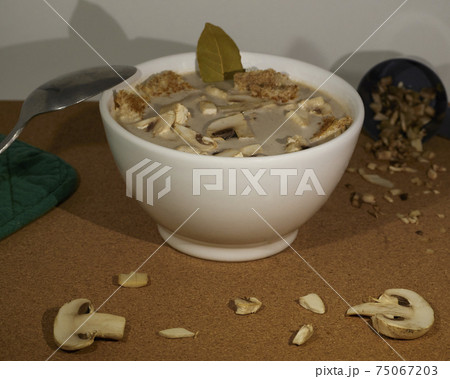 Delcious mushroom cream soup with mushrooms, croutons and a bay leaf decorated with mushrooms in a white bowl 75067203