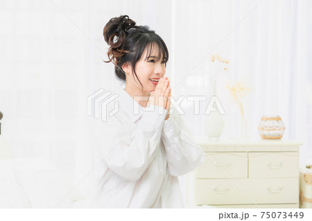 部屋でお願いのジェスチャーをする白いシャツを着た若い女性 75073449