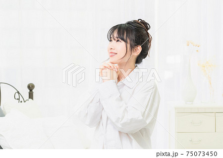 部屋でお願いのジェスチャーをする白いシャツを着た若い女性 75073450