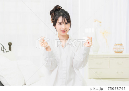 部屋でハートの形を作る白いシャツを着た若い女性 部屋でハートの形を作る白いシャツを着た若い女性 75073745
