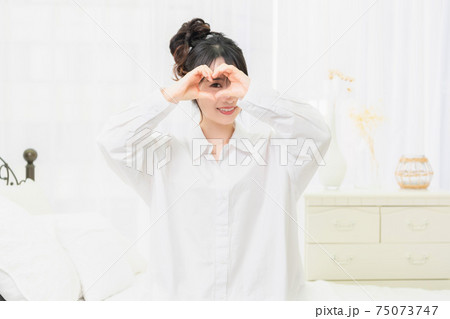 部屋でハートの形を作る白いシャツを着た若い女性 75073747
