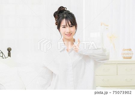 部屋で、いいねのジェスチャーをする白いシャツを着た若い女性 部屋で、いいねのジェスチャーをする白いシャツを着た若い女性 75073902