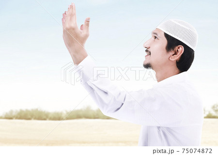Asian Muslim man standing while raised hands and praying Asian Muslim man standing while raised hands and praying 75074872