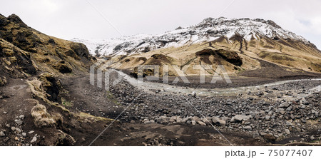 Mountain river at the foot of the mountain with a snow-capped peak. Yellow dry grass on the mountains in May in Iceland. Mountain river at the foot of the mountain with a snow-capped peak. Yellow dry grass on the mountains in May in Iceland. 75077407