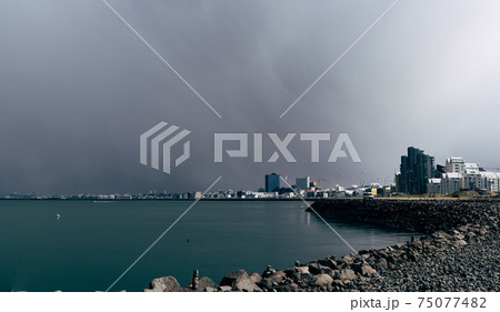 Multi-storey modern high-rise buildings on the waterfront in Reykjavik, the capital of Iceland. The shore of the Atlantic Ocean, the quiet water is calm. Cloudy sky, a blizzard is approaching. 75077482
