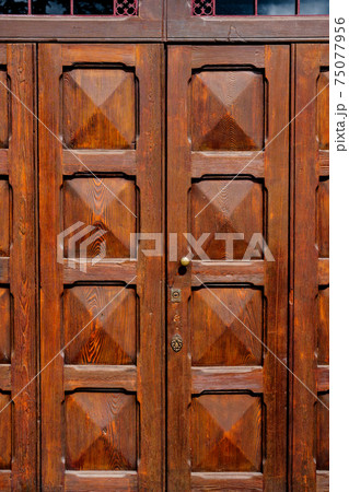 Brown wooden doors with convex squares under a metal grille at the entrance. Brown wooden doors with convex squares under a metal grille at the entrance. 75077956