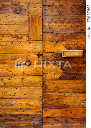 Close-up of the old wooden door of boards with latks with a metal ring handle and a mail hole. Close-up of the old wooden door of boards with latks with a metal ring handle and a mail hole. 75077965