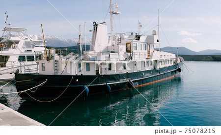 A metal longboat moored in the port of Lustica Bay, against the backdrop of the snow-capped peaks of Mount Lovcen in Montenegro. 75078215