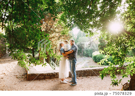 Happy family - mom and dad are holding a little son in their arms in the park among beautiful trees 75078329