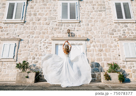 A bride in a wedding dress is spinning on the old street of Perast, her skirt flutters in the wind  75078377