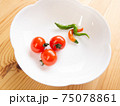 白木のテーブルの上の白いお皿にのったプチトマトと二色のとうがらし 75078861