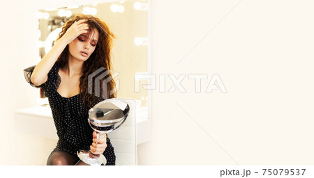 Beautiful girl model brunette, looks in the mirror straightens her hair in a beauty salon. Young Beautiful girl model brunette, looks in the mirror straightens her hair in a beauty salon. Young 75079537