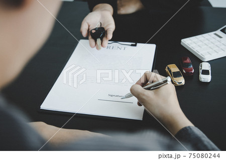 Female attendant handed over the rental car key to the customer who signed the contract and the terms of the agreement on the document, Car rental service concept. 75080244