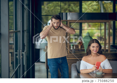 Woman with smartphone and man touching hands to head 75086250