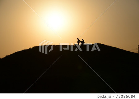 暮れなずむ古墳を散策する人たちのシルエットの美しい風景 75086684