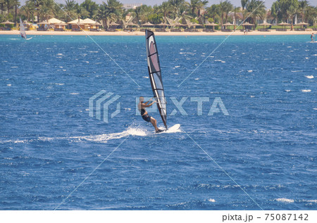 the windsurfer on the board under sail moves at a speed along the surface of the sea 75087142