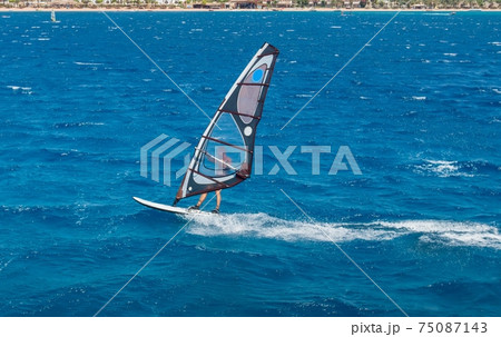 the windsurfer on the board under sail moves at a speed along the surface of the sea the windsurfer on the board under sail moves at a speed along the surface of the sea 75087143