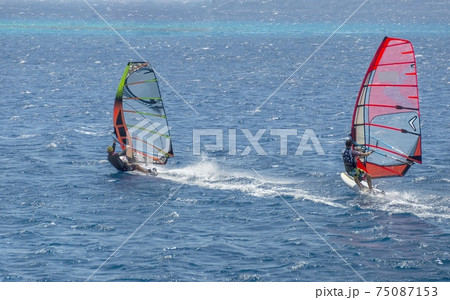 two windsurfers on sailboards are moving at a speed along the sea surface 75087153