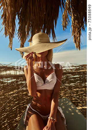 Woman sitting at Cabana with straw roof on a sandy beach on sunny day at Red Sea Woman sitting at Cabana with straw roof on a sandy beach on sunny day at Red Sea 75088649