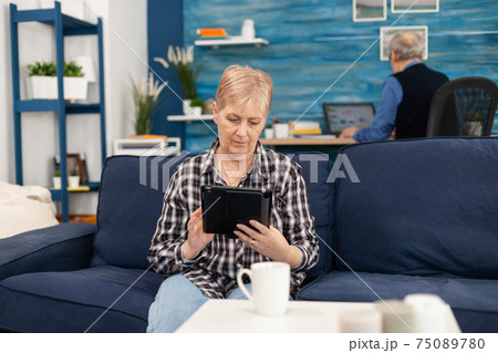 Middle aged lady relaxing on sofa reading on tablet pc 75089780
