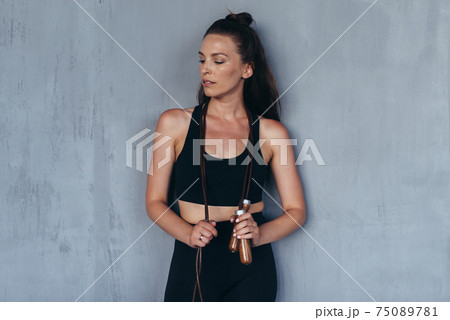 Portrait of a sporty girl with a skipping rope standing against the wall 75089781