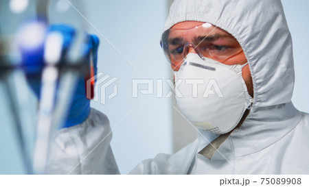Close up of chemist holding blood sample wearing coverall Close up of chemist holding blood sample wearing coverall 75089908