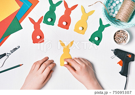DIY Easter home decor from natural materials. Hands make garland of colored paper, twine and pom-poms 75095307