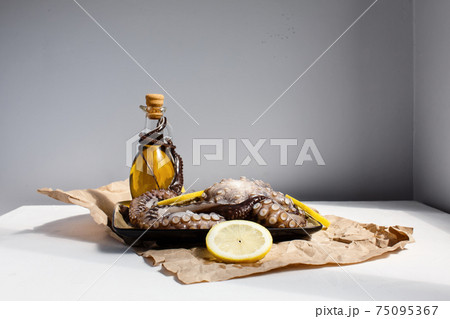 Seafood, whole raw big octopus on a plate with lemons and olive oil ready for preparing 75095367