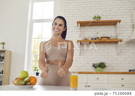 Happy slender female athlete raises thumbs up showing that fresh fruit juice and fruit is super. Happy slender female athlete raises thumbs up showing that fresh fruit juice and fruit is super. 75100088