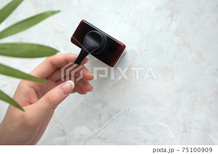 Female hand on body lotion brown container on marble background with copy space 75100909