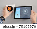 Man is Adjusting a  temperature using a tablet with a smart home app in modern living room 75102970