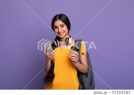 Indian female student holding mobile phone and coffee 75103585