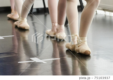 Tying her slippers before performance. Close-up of young ballerina in white tutu tying her slippers while sitting. Tying her slippers before performance. Close-up of young ballerina in white tutu tying her slippers while sitting. 75103937