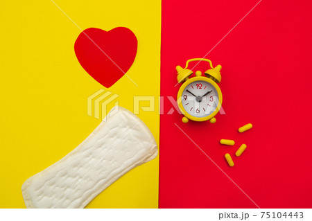 Sanitary pads, alarm clock and hormonal contraceptive pills on colorful background. Female's menstrual cycle concept. Pain relievers for menstrual pain 75104443
