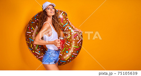 Young woman girl posing with donut-shaped swim inflatable ring isolated on yellow background. Young woman girl posing with donut-shaped swim inflatable ring isolated on yellow background. 75105639