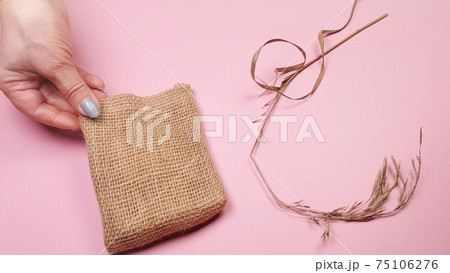 Florist hands prepare dry grass and canvas bag for composition, on pink background, DIY concept Florist hands prepare dry grass and canvas bag for composition, on pink background, DIY concept 75106276