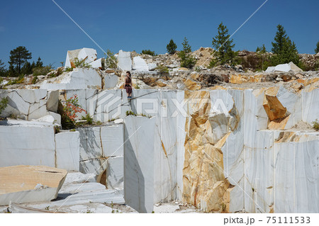 Girl sits on the edge of huge marble quarry Girl sits on the edge of huge marble quarry 75111533