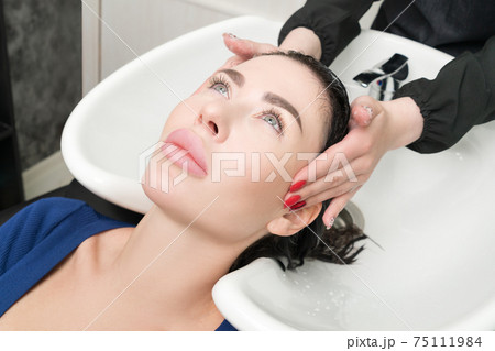 Hairstylist's hands wash long hair of brunette woman with shampoo in special sink for shampooing 75111984