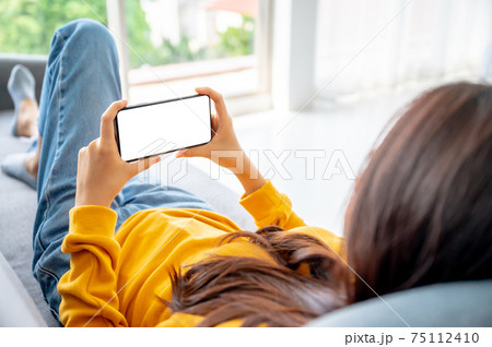 Woman using smart phone and relaxing on sofa Woman using smart phone and relaxing on sofa 75112410