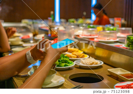 Young people using smartphone while eating at conveyor belt hotpot restaurant 75123098